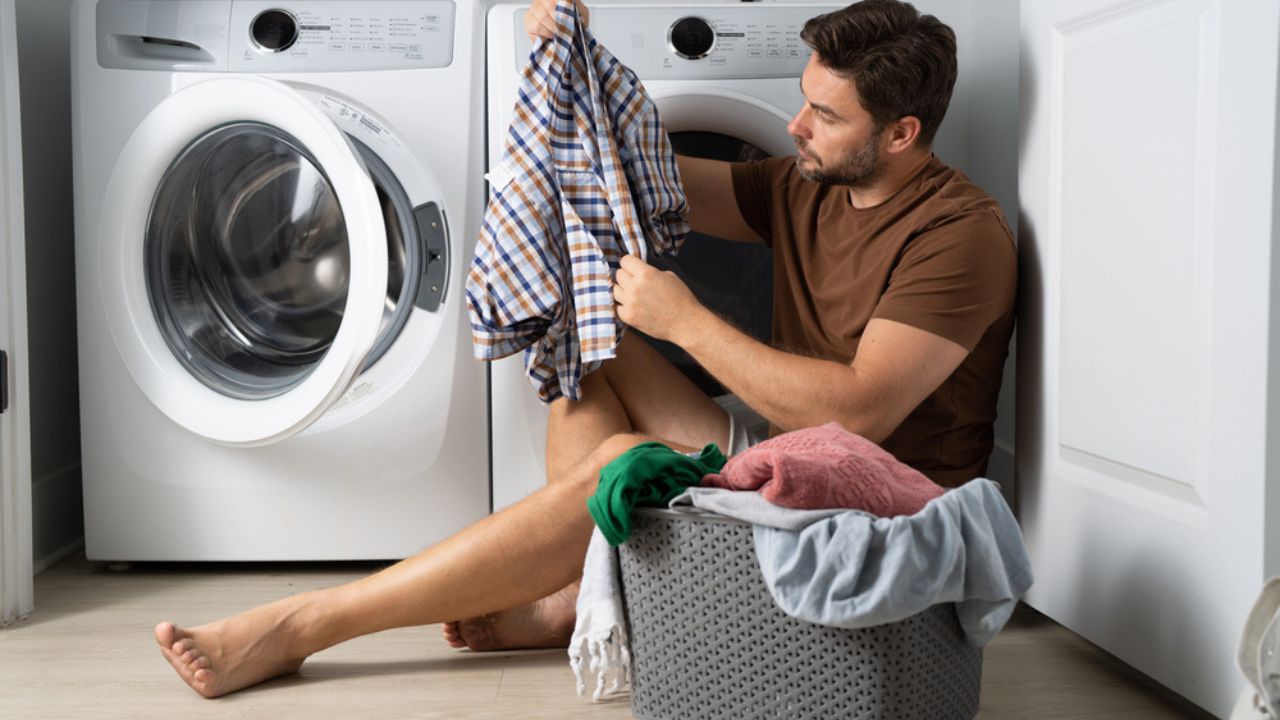 Happy man sorting clothes near washing machine in laundry room