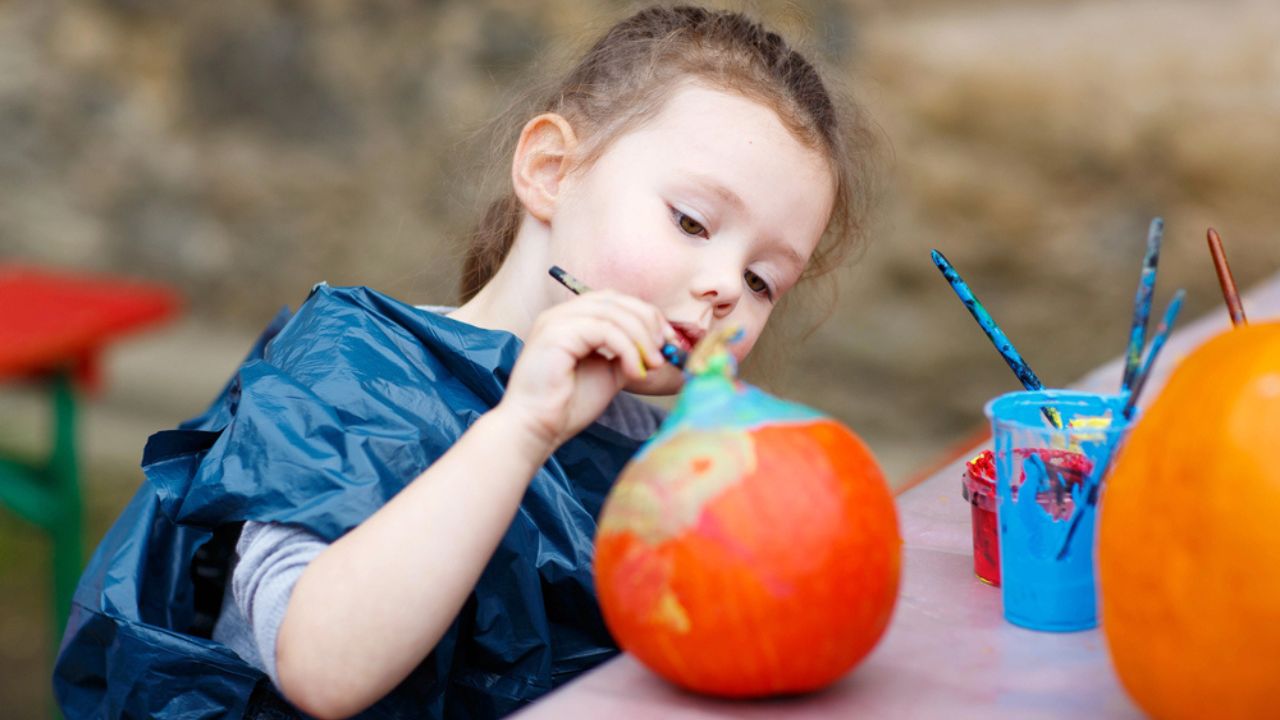 Little kid girl painting with colors on pumpkin
