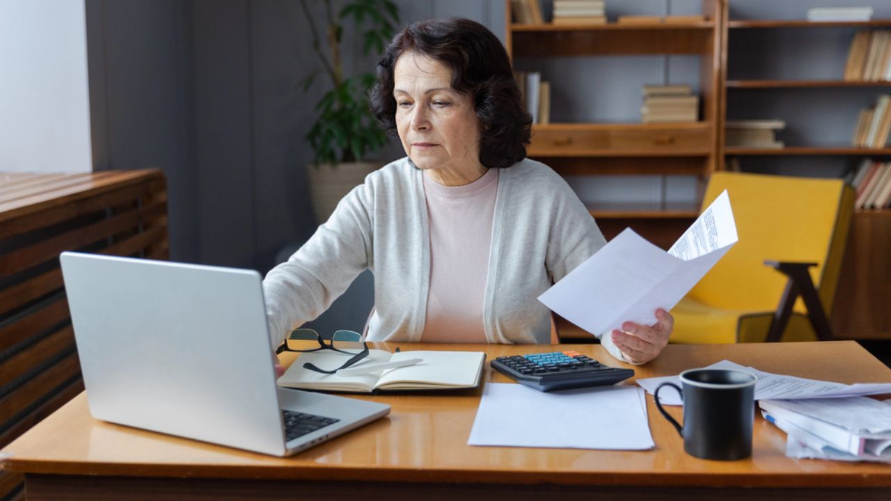 Pensive older mature lady reading paper bill pay online at home managing bank finances calculating taxes planning loan debt pension payment