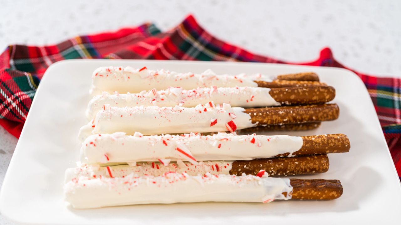 Pile of homemade candy cane chocolate-covered pretzel rods on a white serving plate.