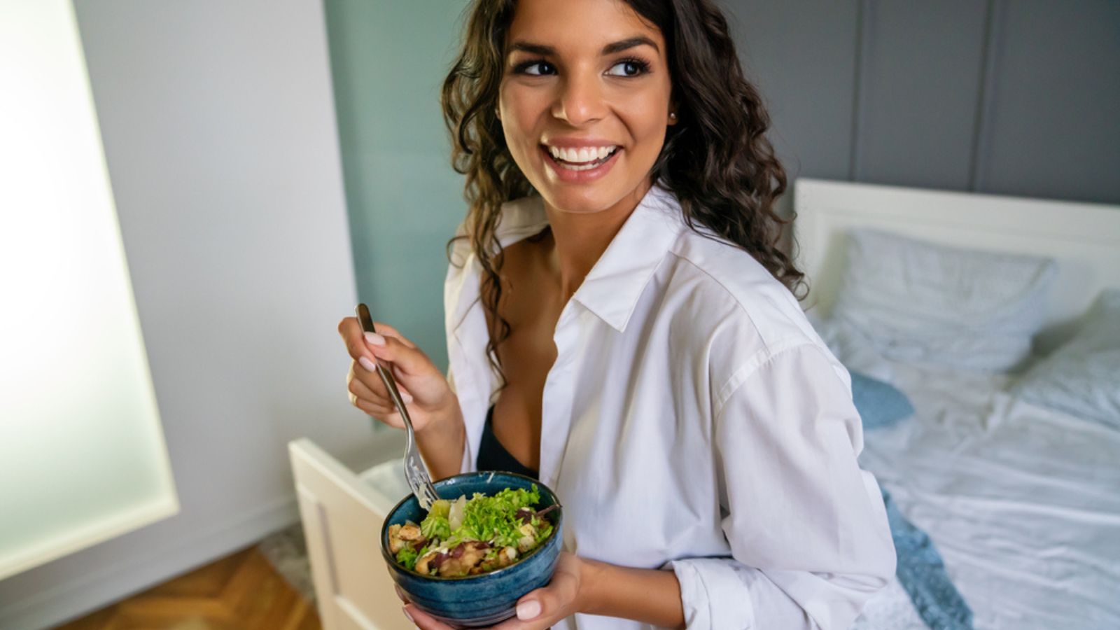 Portrait of a sexy young happy woman eating healthy salad in bedroom. Healthy food diet concept