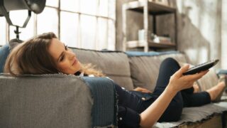 Relaxed woman lying on sofa and watching tv in loft apartmen