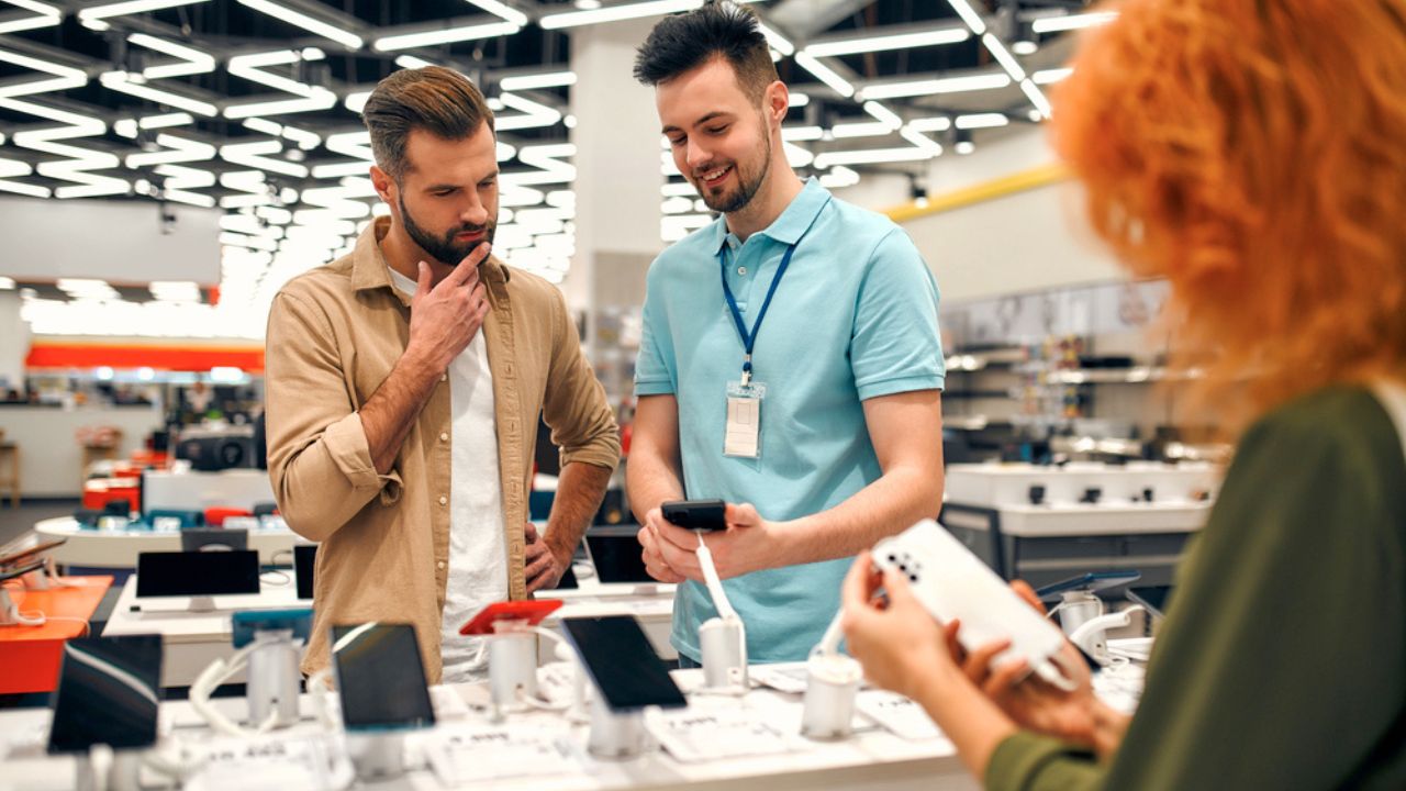 Sales consultant advises man who chooses new smartphone in store of household appliances, electronics and gadgets. Professional consultation in store. Sale Day.