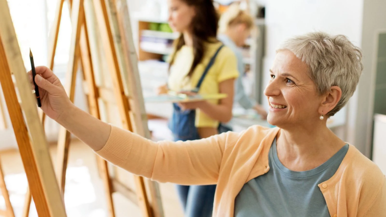 Senior woman drawing painting on easel at art school studio