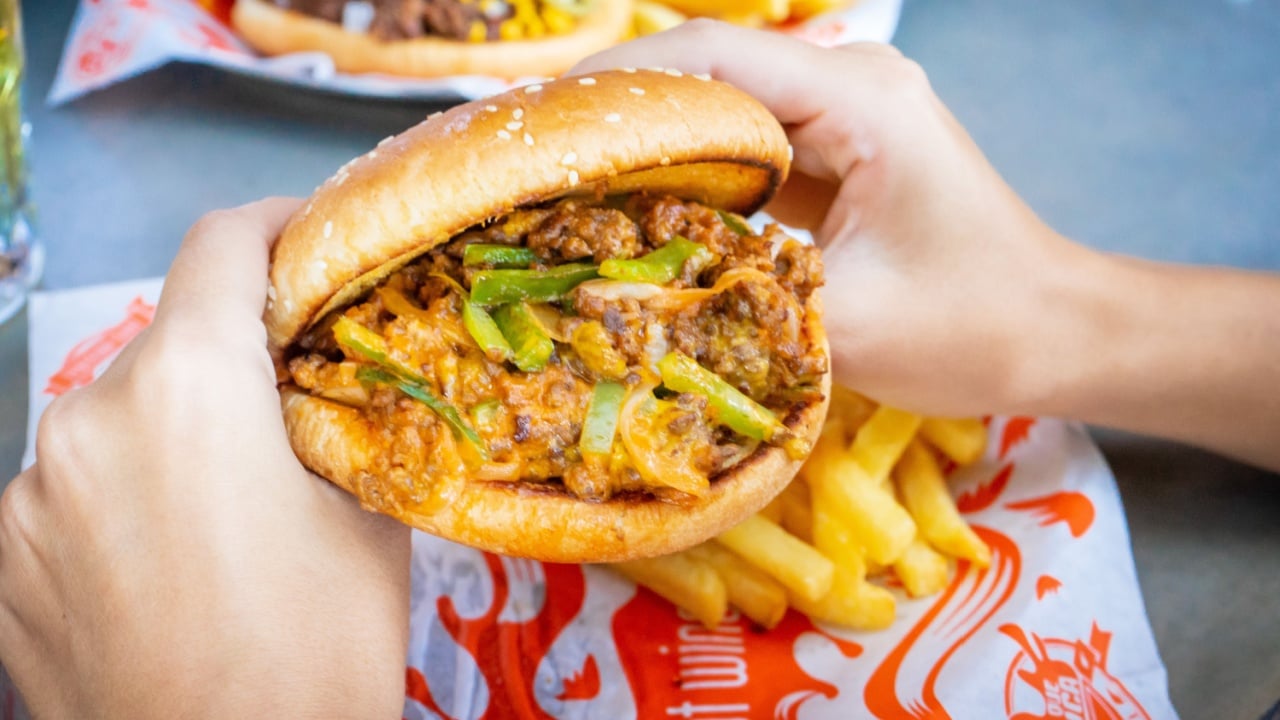 Woman's hands eating a ground beef burger in a restaurant.