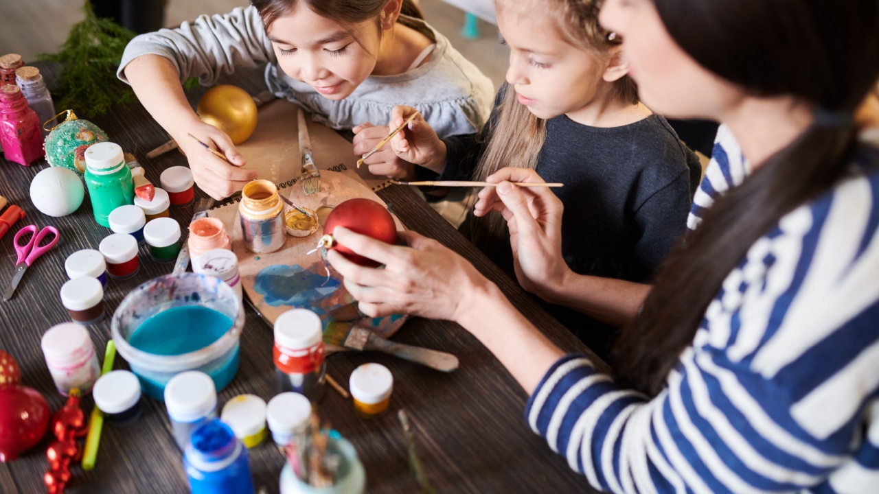 High angle portrait of two little girls painting Christmas baubles in crafting class with teacher helping them