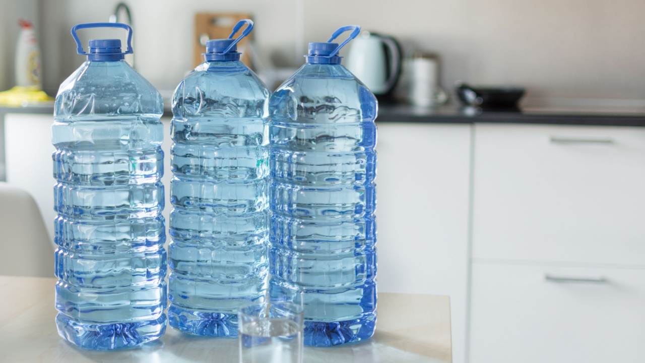 Big plastic bottle with water on the table over bright kitchen backgroung. Bottle of clear transarent water in a blue color cap and handle closeup.
