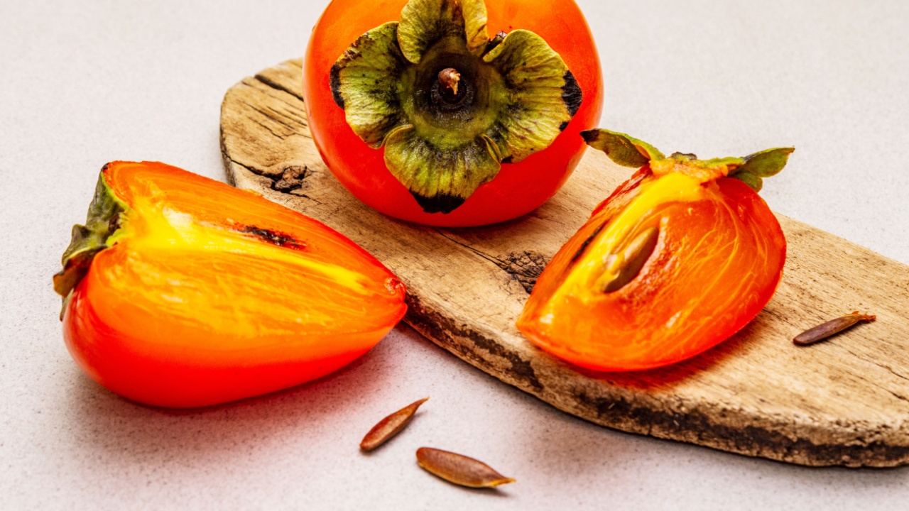Ripe single persimmon. Fresh whole fruit, half sliced, seeds. Wooden cutting board, stone concrete background, close up