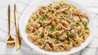 a plate of roasted turkey breast tetrazzini served on a white plate with golden fork and knife on a wooden table
