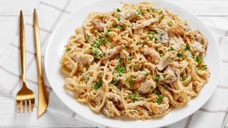 a plate of roasted turkey breast tetrazzini served on a white plate with golden fork and knife on a wooden table
