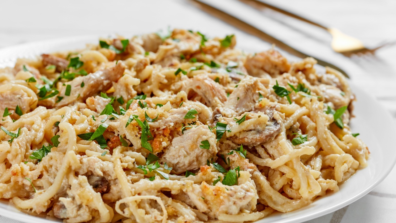 close-up of roasted turkey breast tetrazzini served on a white plate with golden fork and knife on a wooden table, american cuisine, horizontal view from above