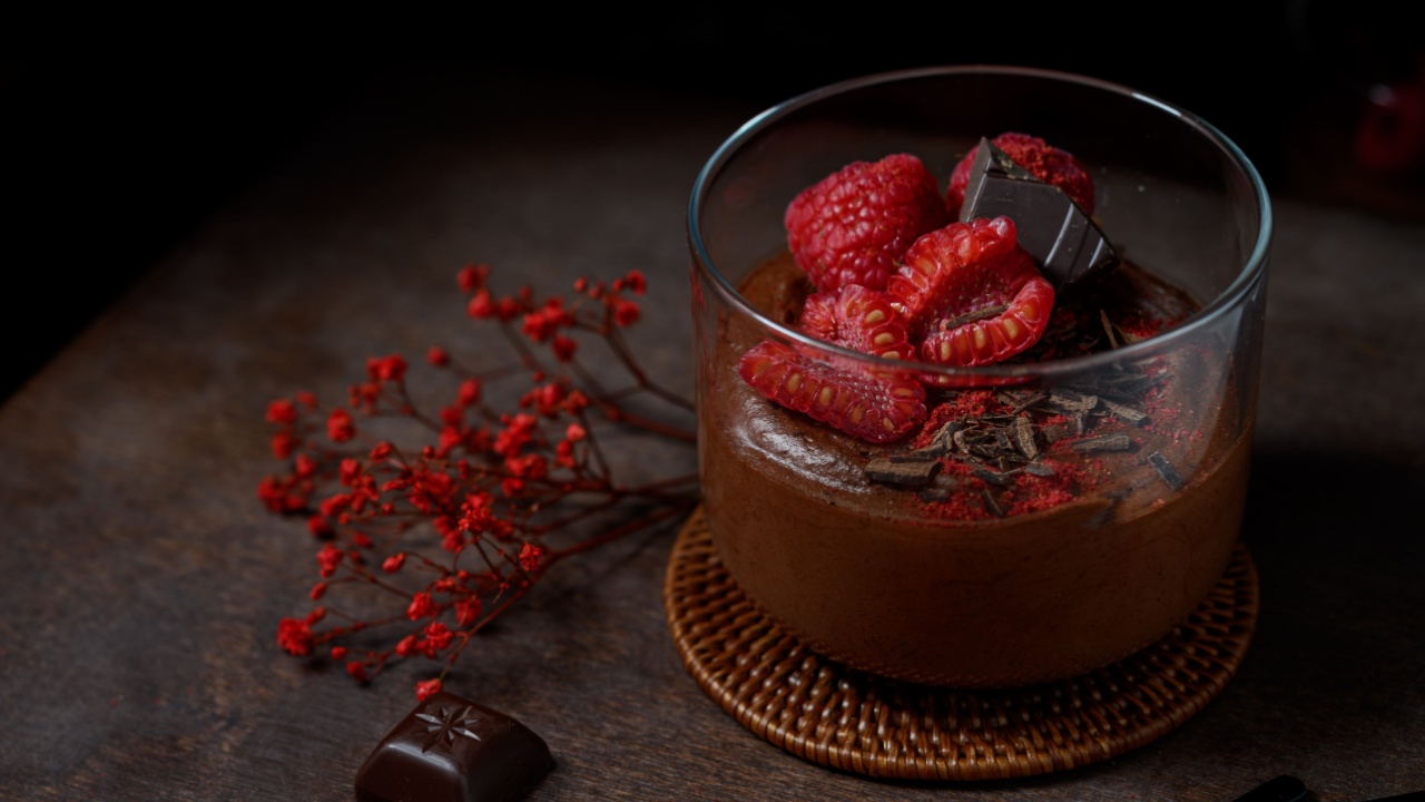 Fluffy vegan chocolate mousse made from aquafaba (chickpea water), vegan dark chocolate and maple syrup - dairy-free, no sugar, fit dessert. Served with raspberries on wooden board. Dark photo.