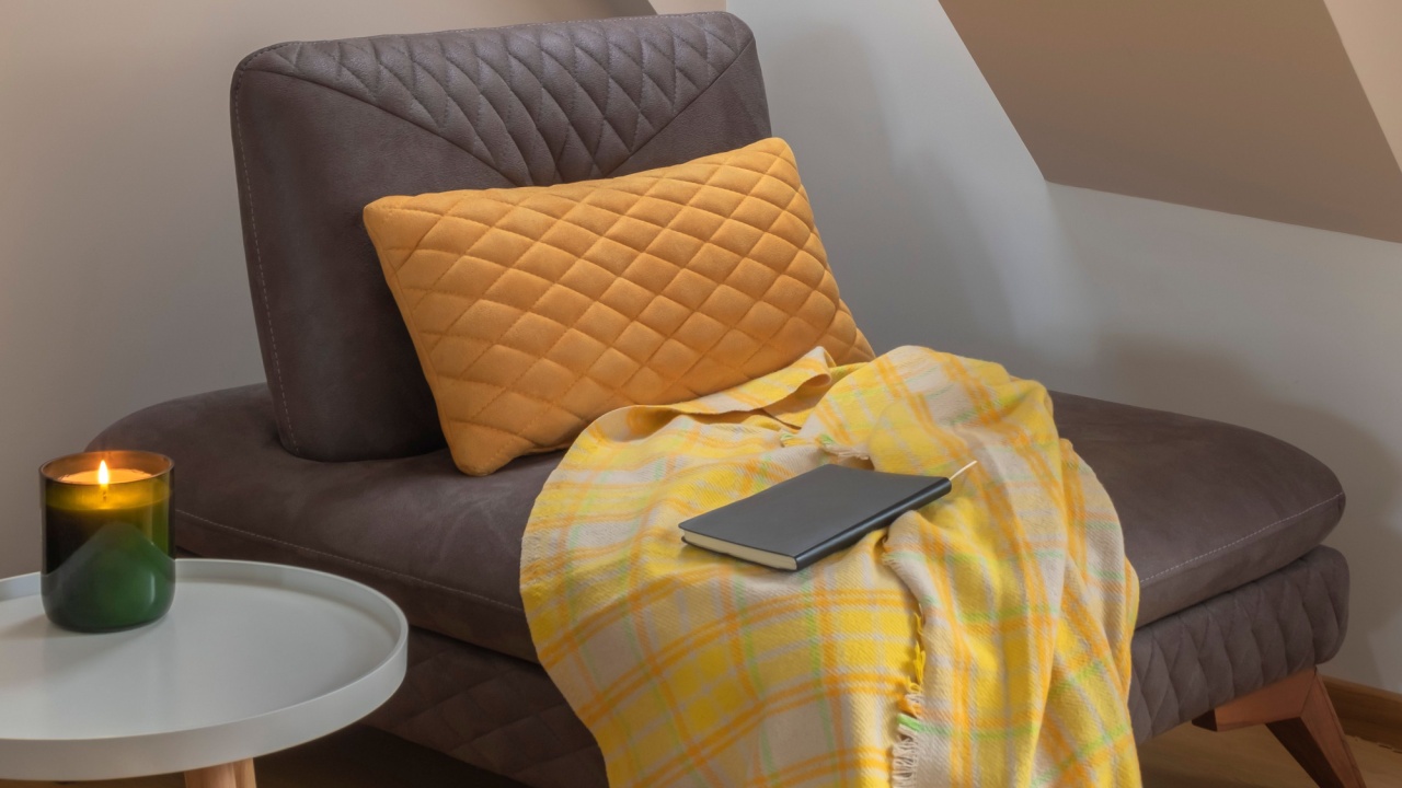 Cozy nook by the window with yellow blanket and pillow on a coach, candle on coffee table and book