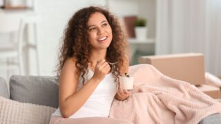 Young woman eating tasty yogurt at home