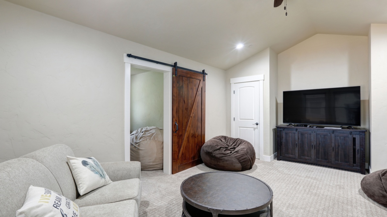 Bright light grey living room with TV, stand and round table with sofa and barn door with light grey carpet.