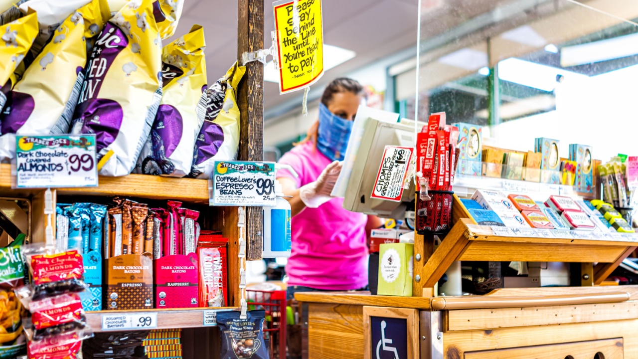 Reston, USA - April 9, 2020: Social distancing sign at cashier check-out aisle inside Trader Joe's grocery shop store during coronavirus with woman employee in mask