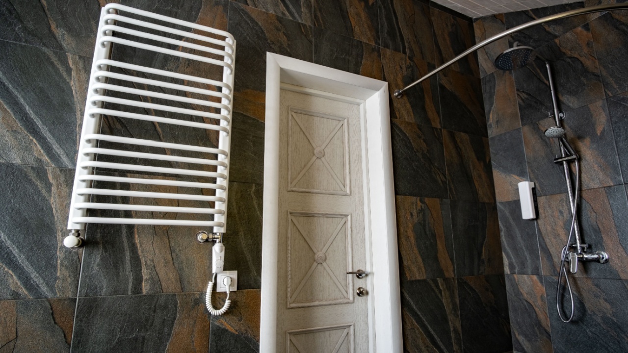 White contemporary electric towel dryer mounted on black tiled wall in modern bathroom.