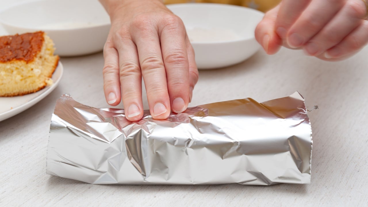 Traditional Brazilian dessert (known as Bolo Gelado) - Making step by step: Woman hand wrapping sliced cake in aluminum foil. Close-up.
