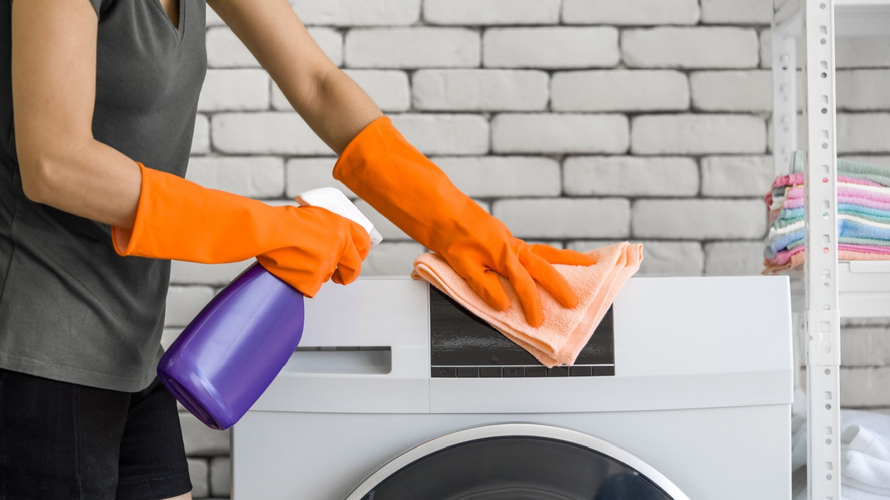 Asian housewife wearing rubber gloves, use a spray and cloth to clean the washing machine. Working atmosphere in the laundry room.