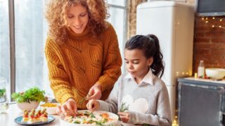 Happy curly woman and mixed race girl niece making healthy vegan salad and snacks for family feasting. Christmas, New year, Thanksgiving, Anniversary, Hanukkah, Mothers day, Easter, engagement concept