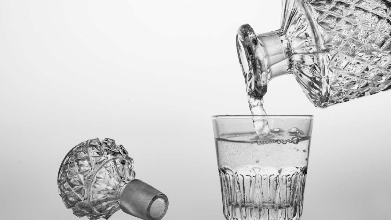 Pouring sparkling water from a carafe into a small glass. Decorative containers for serving water and alcohol. Light background.
