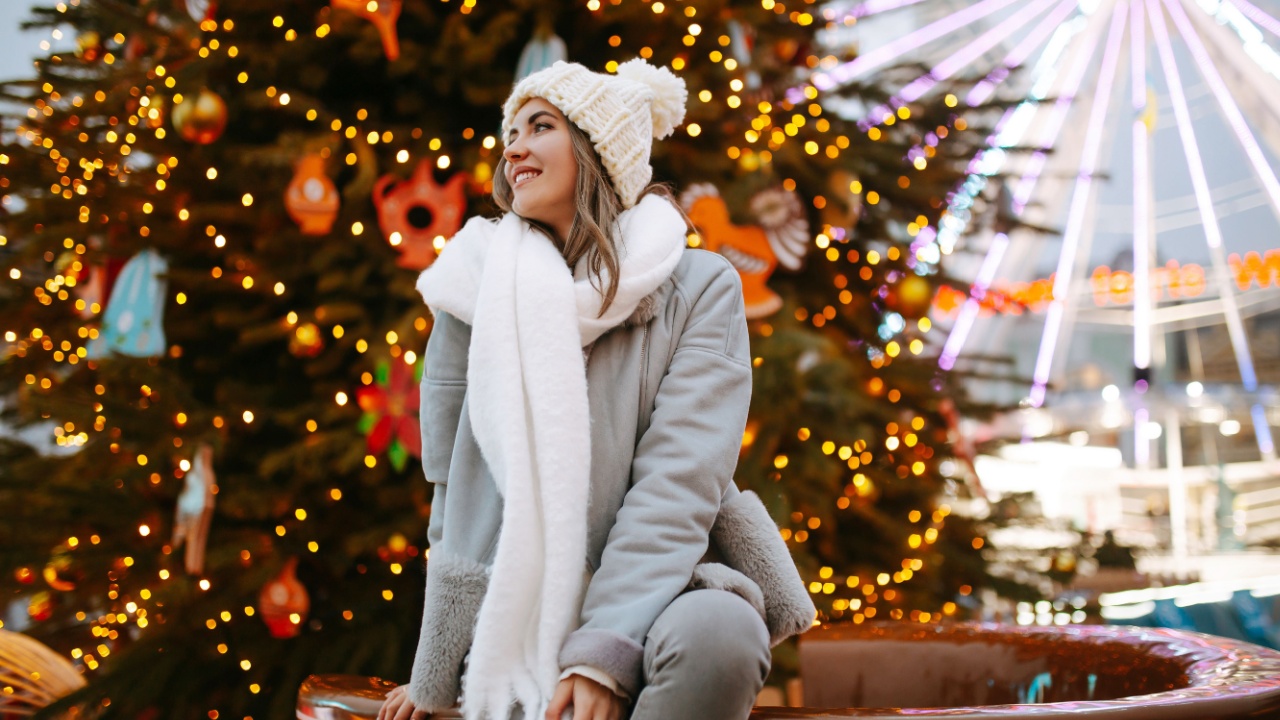 Beautiful woman enjoys winter holidays walking on Christmas market. Young woman posing on festive street. New year.
