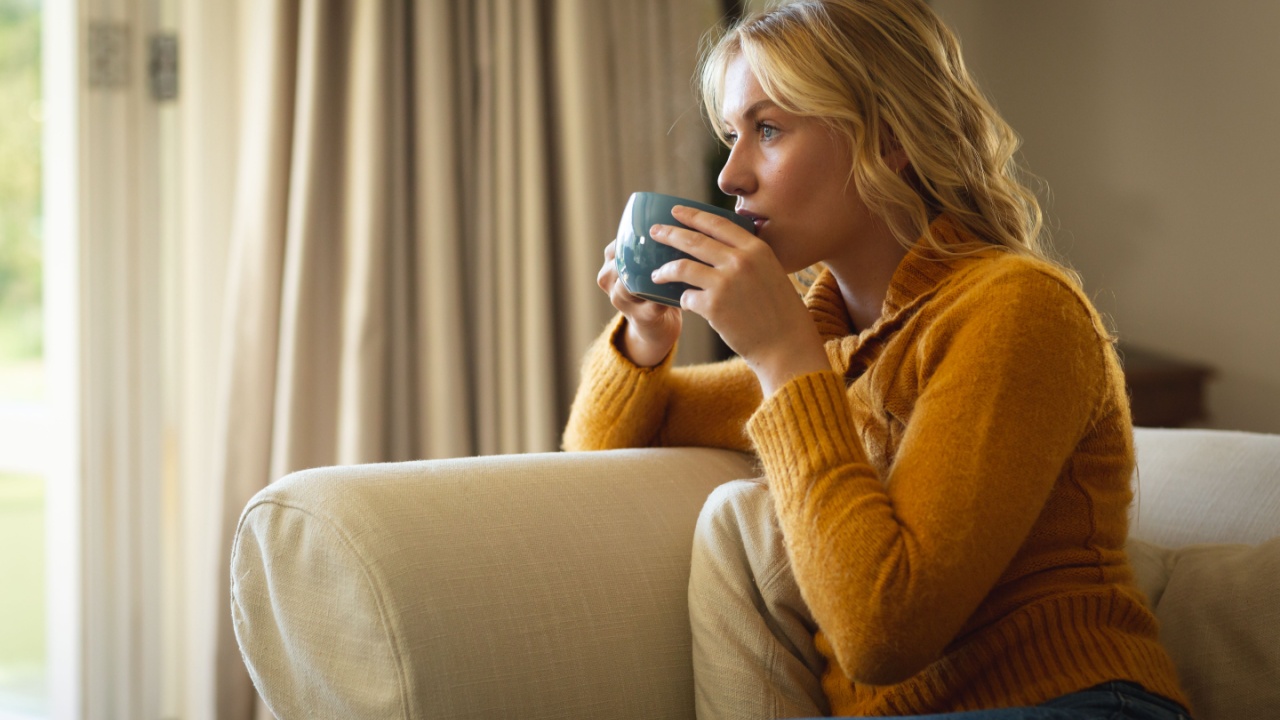 Thoughtful caucasian woman sitting on couch in living room drinking coffee. spending free time at home.