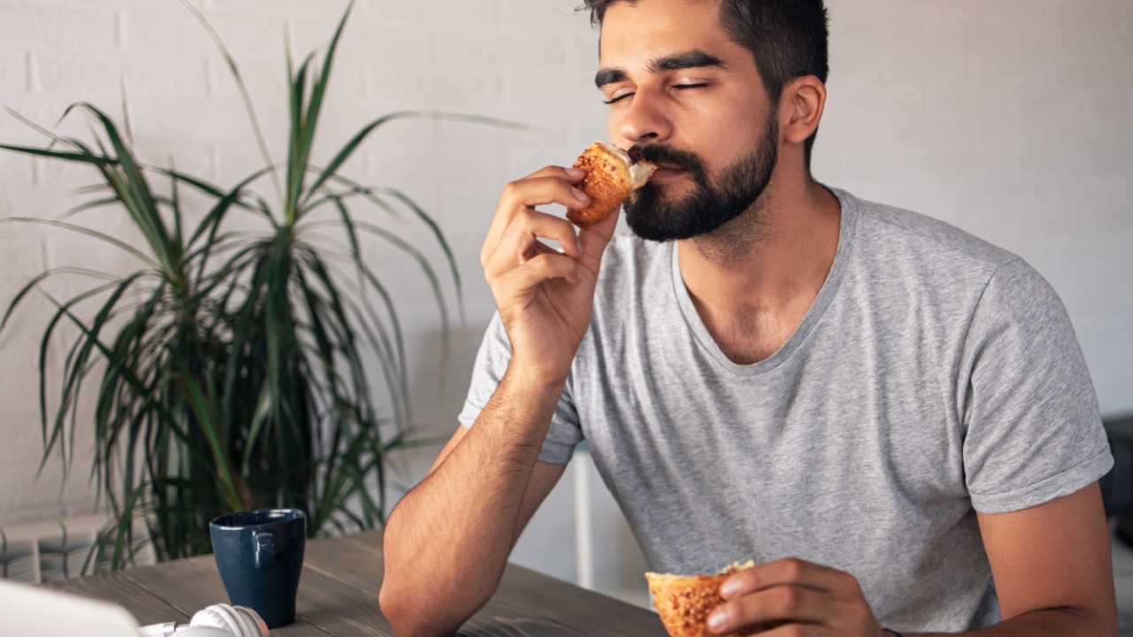 Good looking bearded freelancer sitting at his home office and enjoying the smell of a fresh croissant
