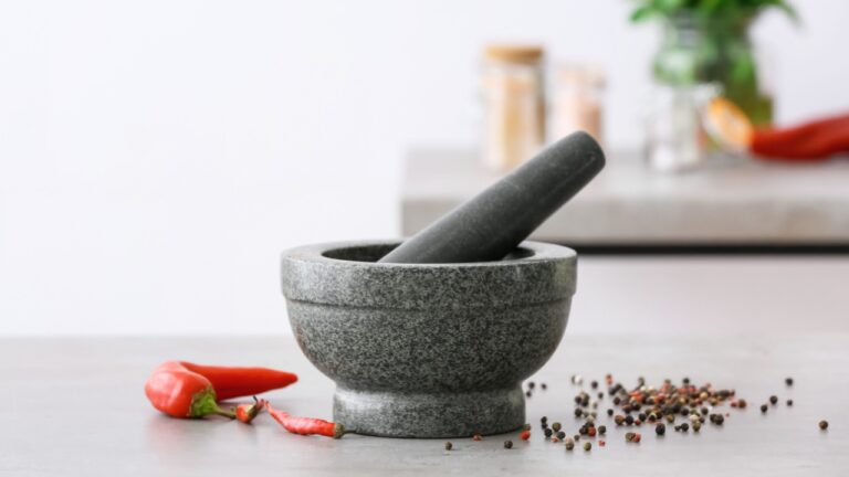 Mortar with spices and pestle on light table in kitchen