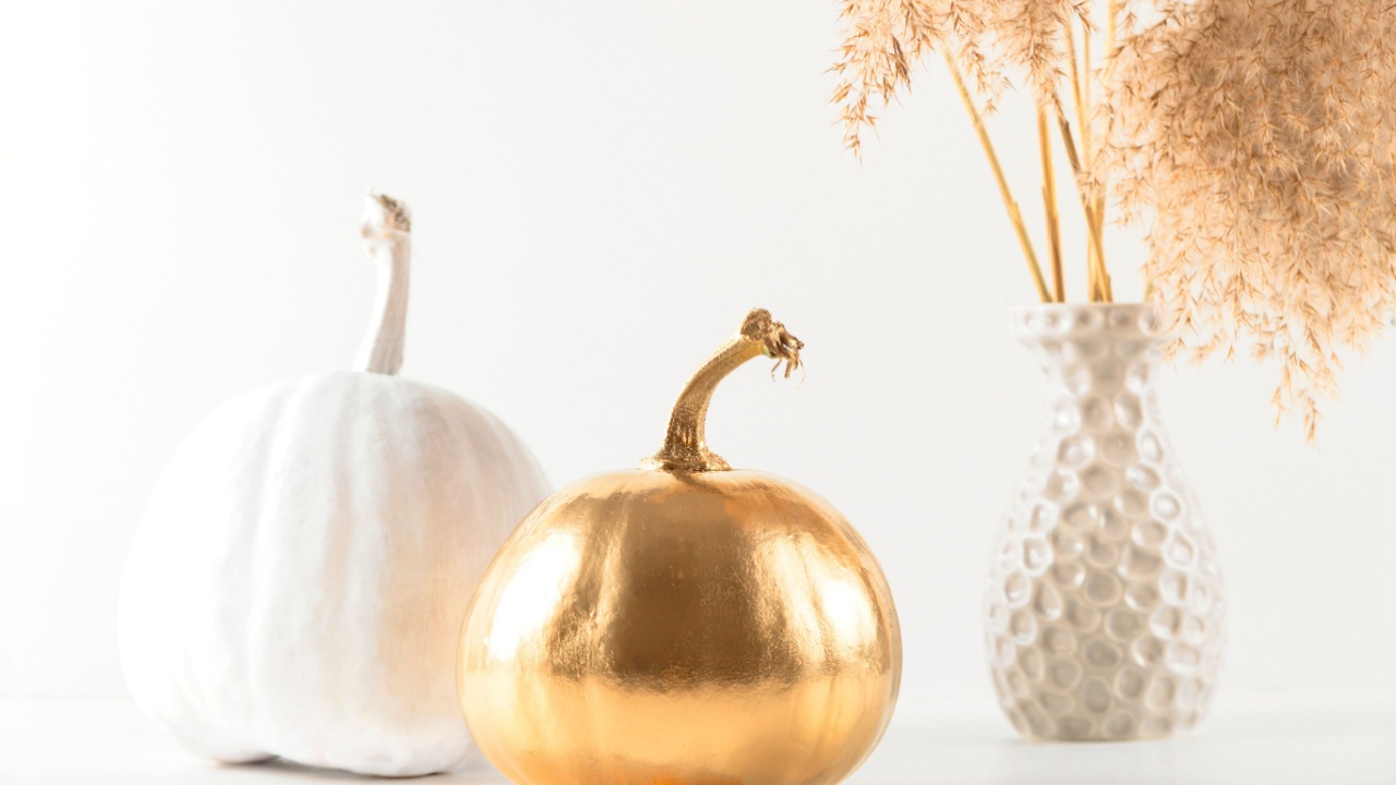 Golden and white decorative pumpkins on a light background next to a vase with pampass grass. Autumn and Halloween cute stylish home decor.