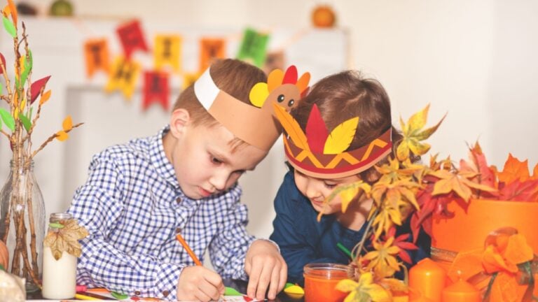 Girl and boy in paper turkey and native American hats writing I am thankful for. Celebrating Thanksgiving day. Diy craft art project.