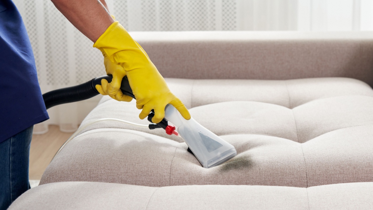 Close-up of housekeeper holding modern washing vacuum cleaner and cleaning dirty sofa with stain with professionally detergent. Professional springclean at home concept