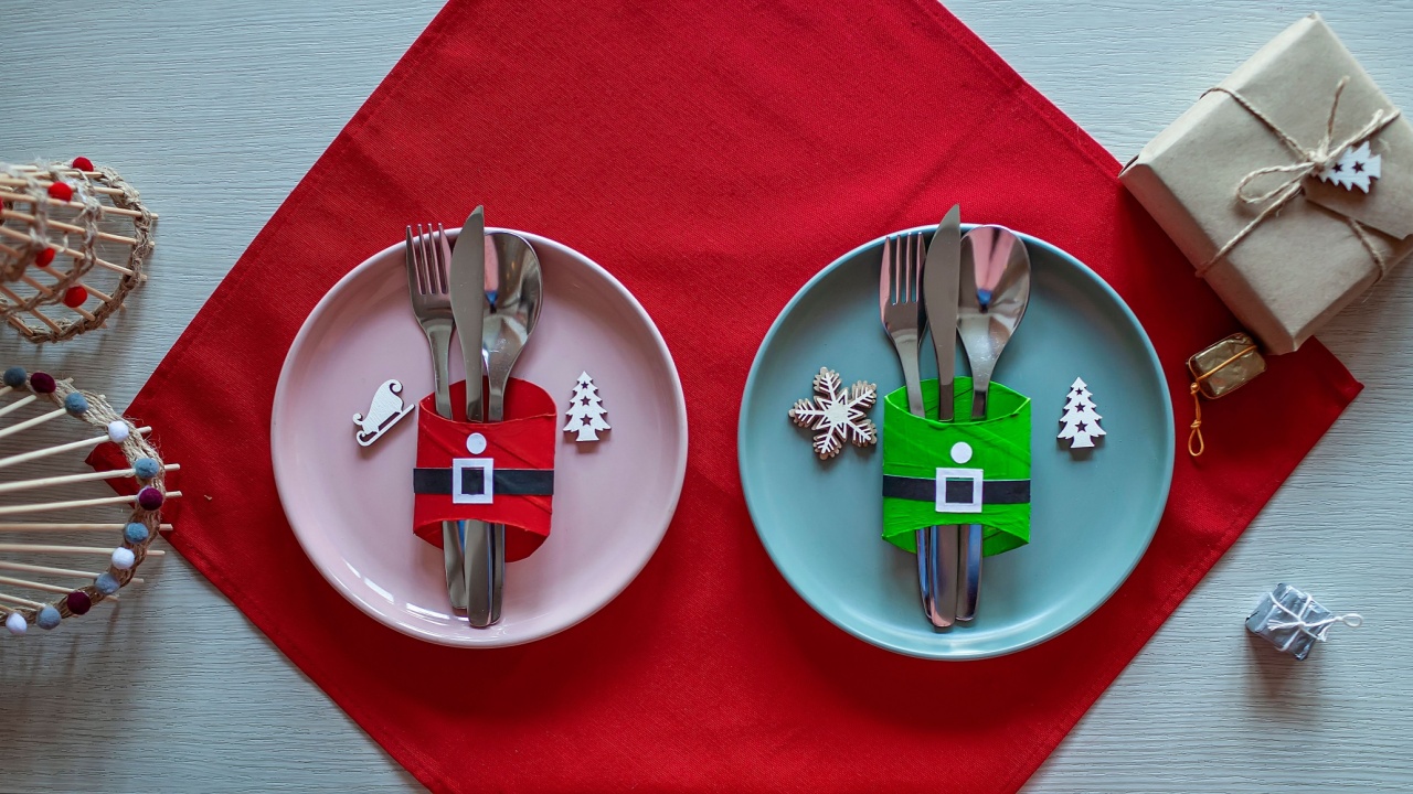 Top view of Christmas tables setting, cutlery and DIY napkin ring holders like Santa clothes made with toilet paper rolls, festive dinner for family with kids. Ecological and sustainable celebration