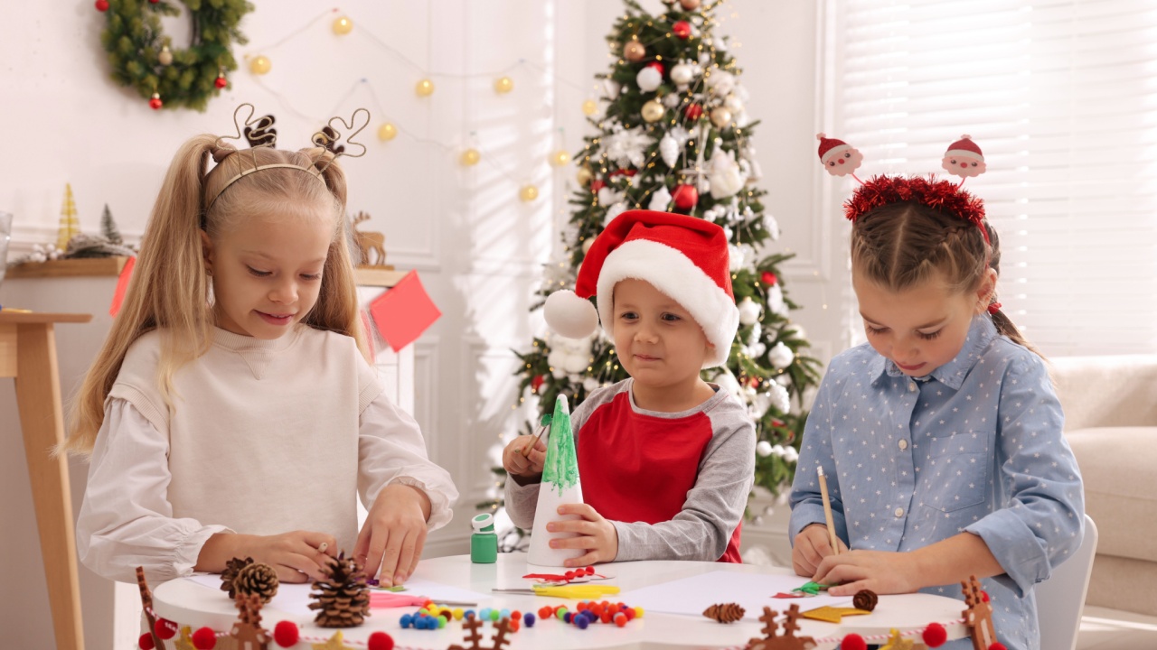 Cute little children making Christmas crafts at table in decorated room