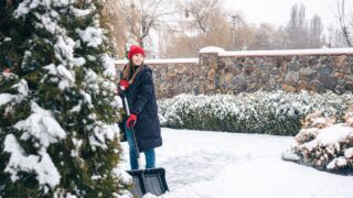 Young woman cleans snow in the yard in snowy weather.