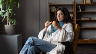 Enjoying seasonal winter fruits. Happy woman eating fresh tangerines has break from work resting in armchair covered with blanket and hold juicy delicious mandarin in hand. Citrus pleasure concept