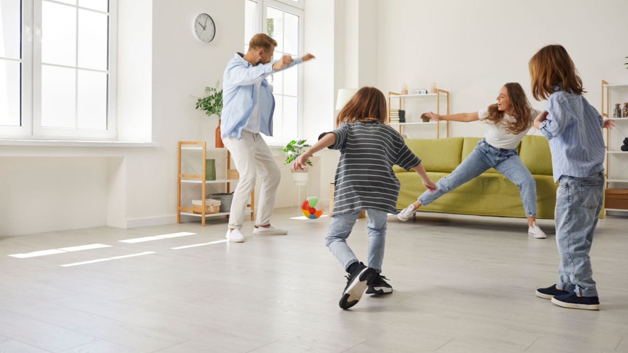 Overjoyed young family with children have fun play football in living room at home. Happy parents with kids enjoy leisure active game on weekend indoors. Entertainment and hobby concept.