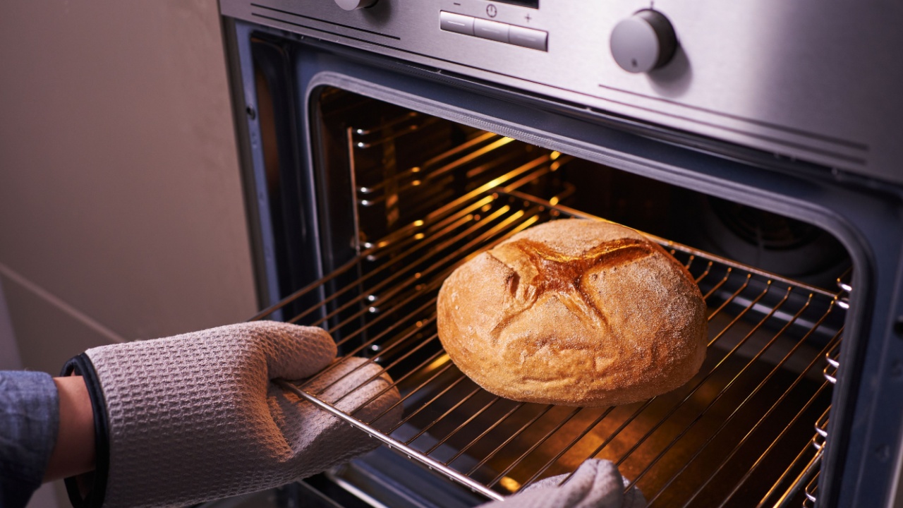 female hands in oven mitts take round bread out of the oven