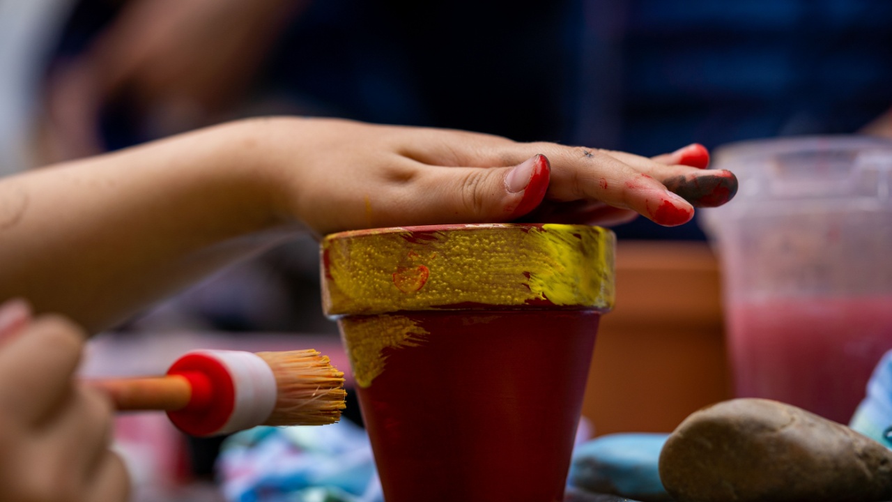 hand of a child with paintbrush, painting a clay pot with acrylic colours, Dirty fingers dyed of tempera paints, creative activities for children, artistic skills development concept