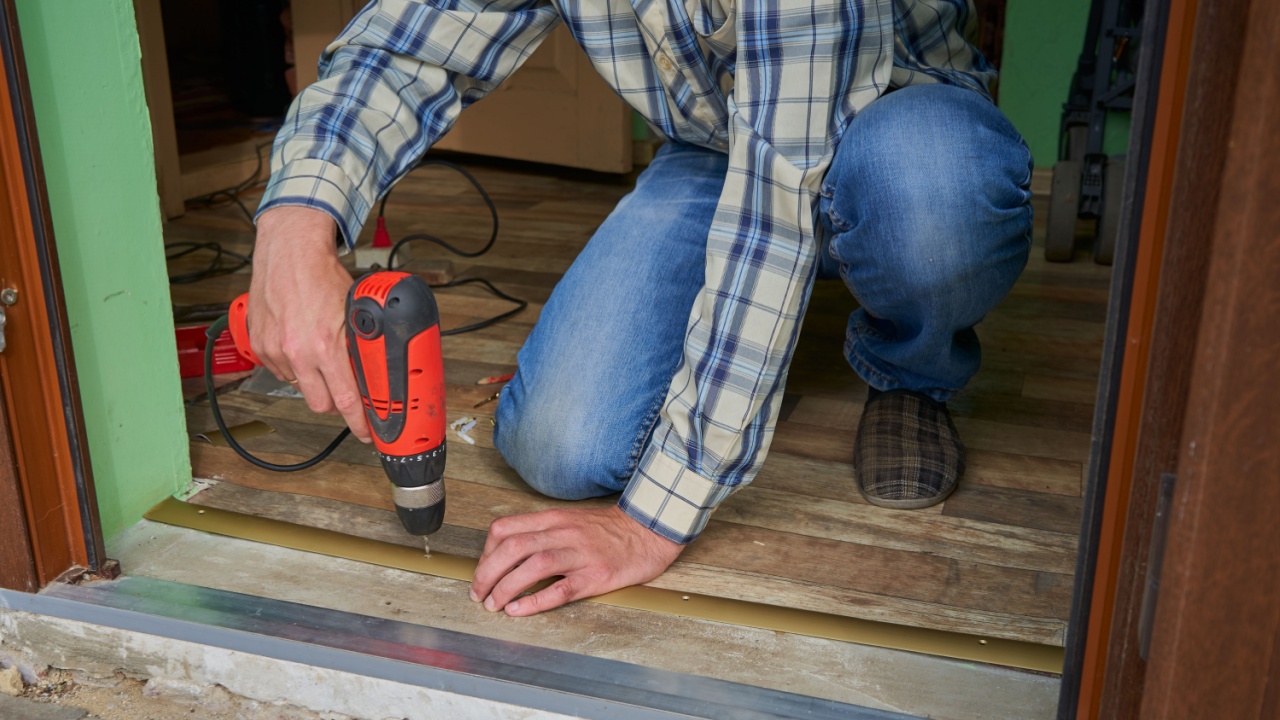 installation in the door of of a threshold,a man drills holes in the door sill, setting the threshold on the laminate