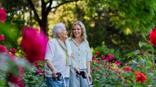 Adult granddaguhter supporting her senior grandmother when taking her for walk with walker in park in summer.