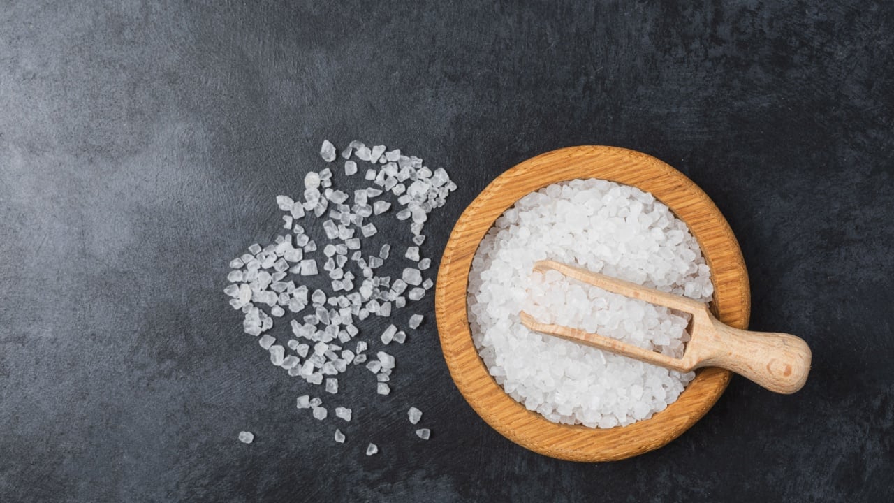 Sea salt in wooden bowl on black table. Top view, flatlay. Food background wit copy space.