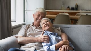 Joyful senior couple enjoy rest and conversation sit on cozy sofa