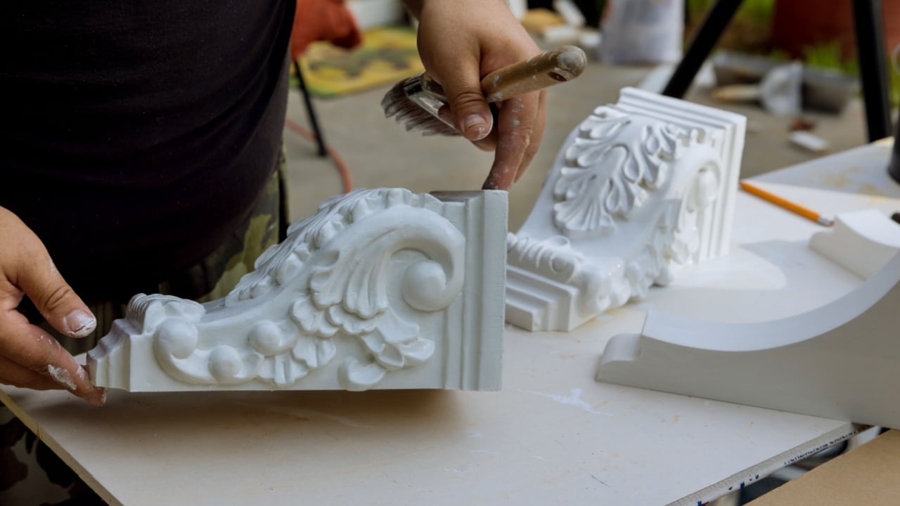 The worker is using a paintbrush to that are paint wooden corbels for the kitchen island