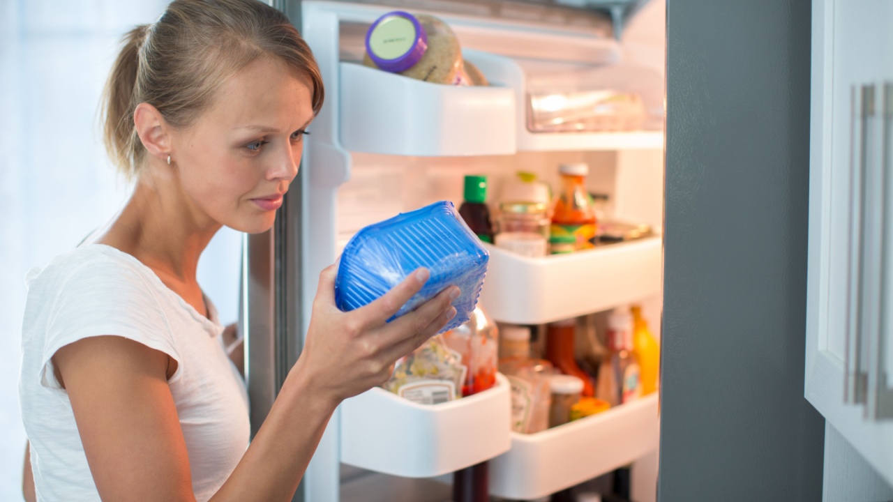 Is this still fine? Pretty, young woman in her kitchen by the fridge, looking at the expiry date of a product she took from her fridge -
