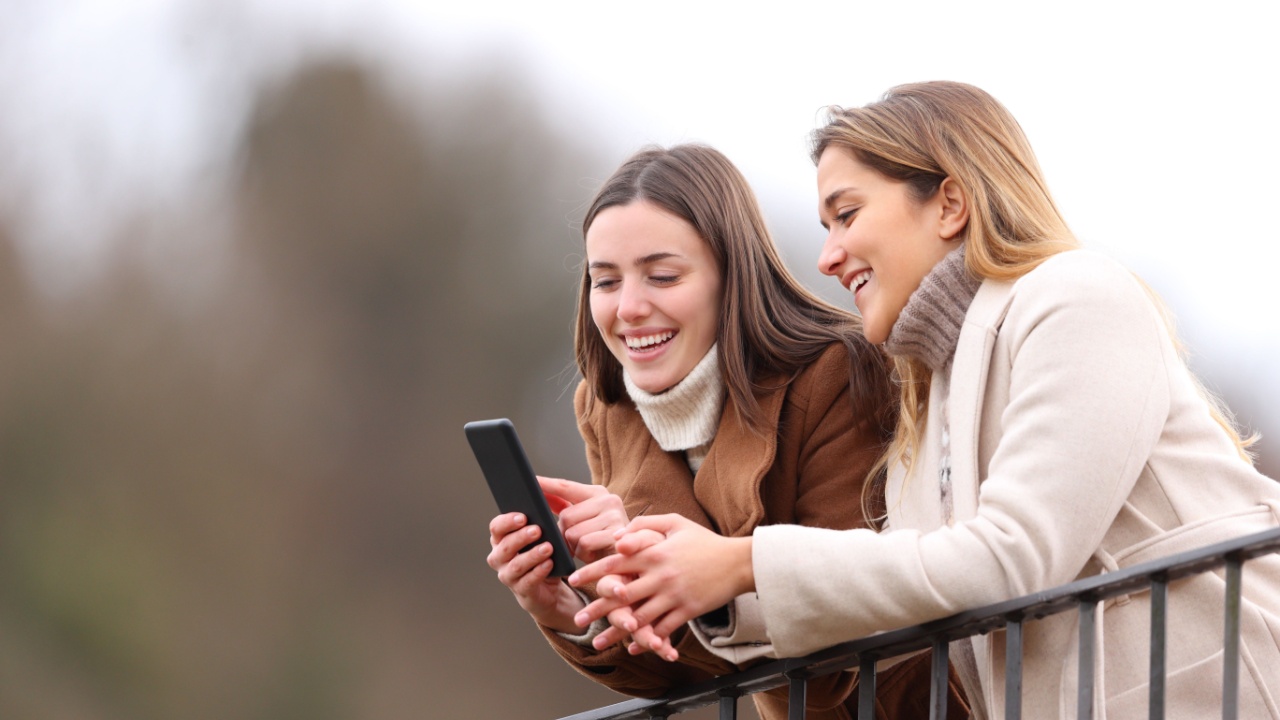 Two happy friends checking smart phone in winter in a balcony