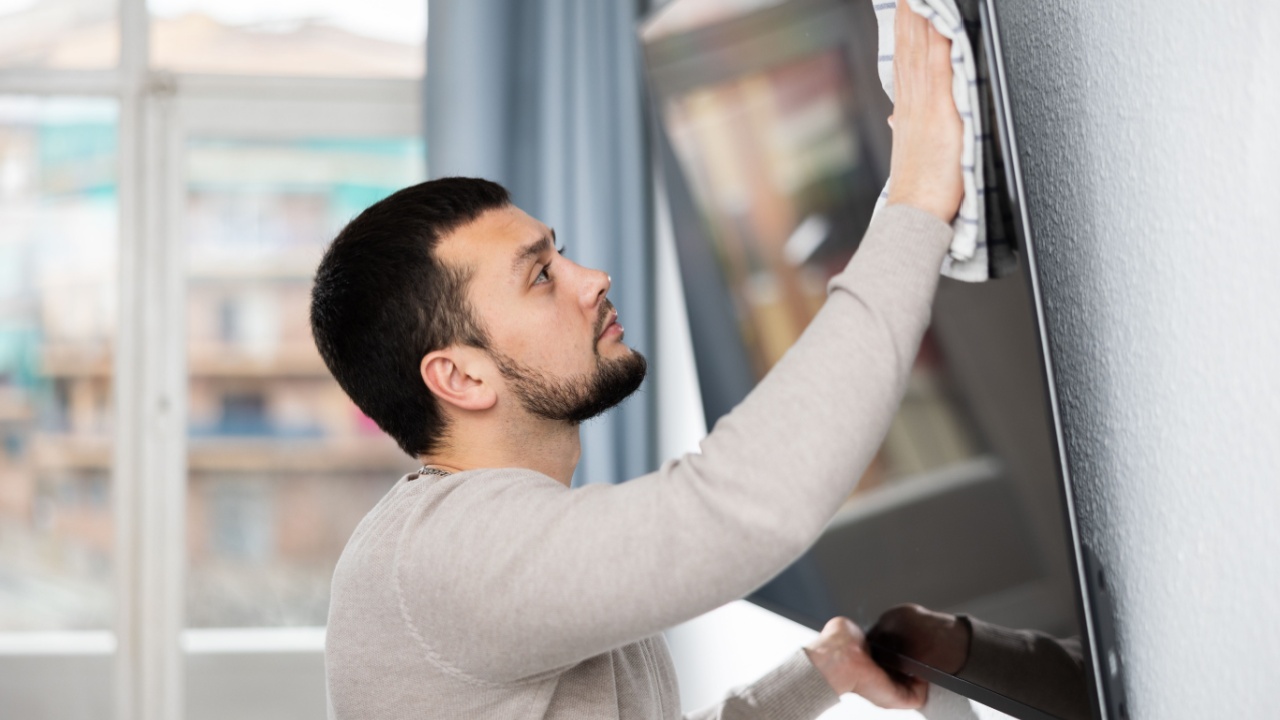 Man wipes a tv in a living room with a rag