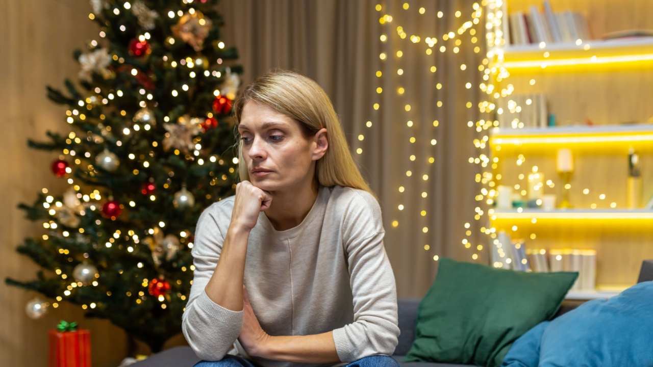 Sad woman alone at home for christmas, sitting on sofa in living room depressed on new year holidays.