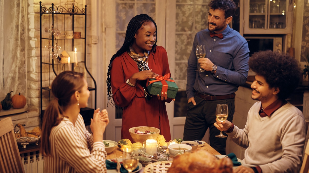 Happy African American woman getting gift from her friends while hosting Thanksgiving dinner in dining room.