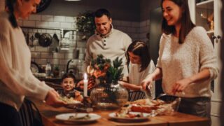 Family preparing traditional festive Christmas Eve dinner together in cozy homely atmosphere, two daughters helping parents to set New Years table, cooking in kitchen decorated for winter holidays